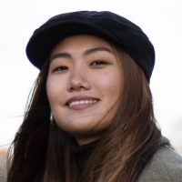 Portrait of a smiling woman wearing a black beret and dark coat, outdoors.